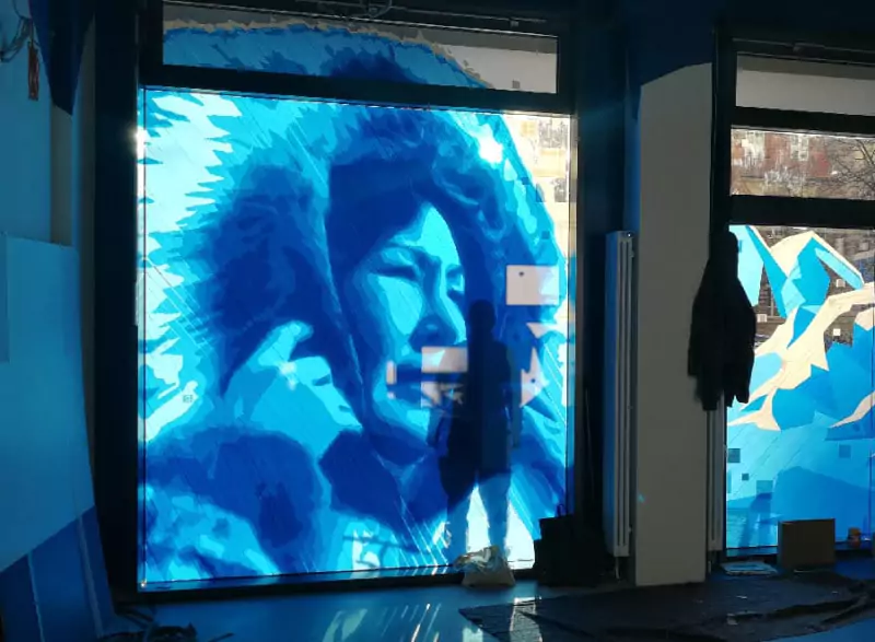 A huge tape art portrait on a shop window made with blue packing tape only